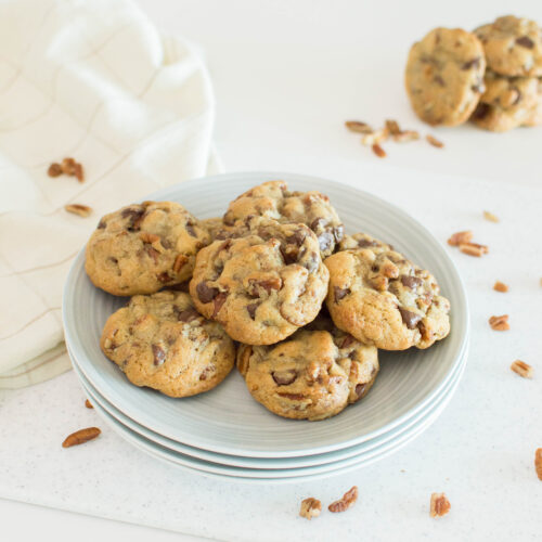 A plate of butter pecan cookies, surrounded by pecans on the table, ready to be served
