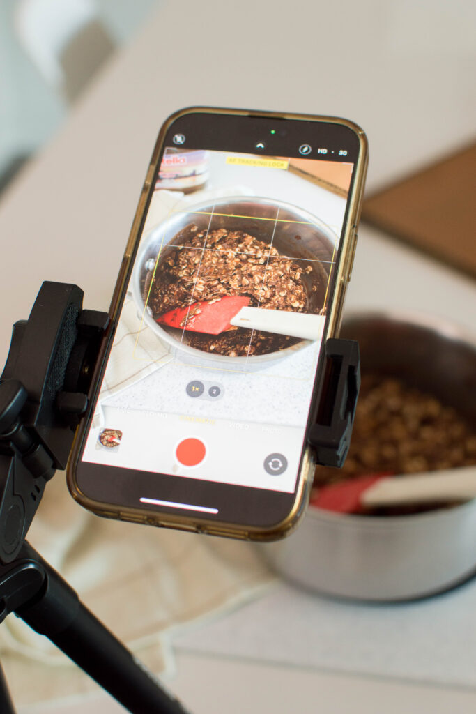 Filming the cookie mixture process with a phone setup in the kitchen.