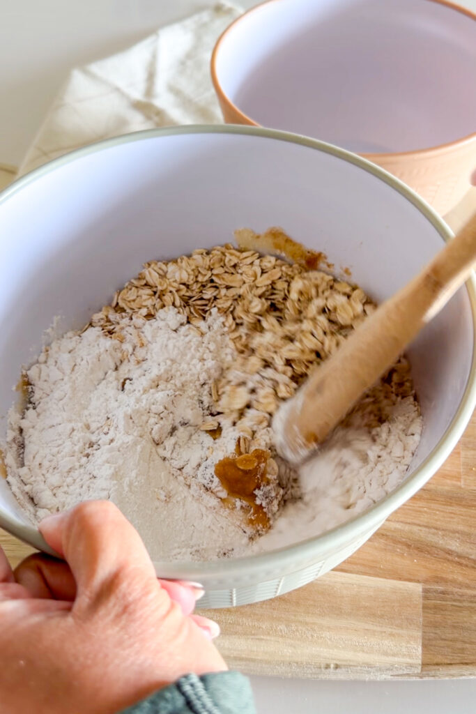 Mixing dry ingredients for apple crumble cookie dough in a white bowl with a wooden spoon.