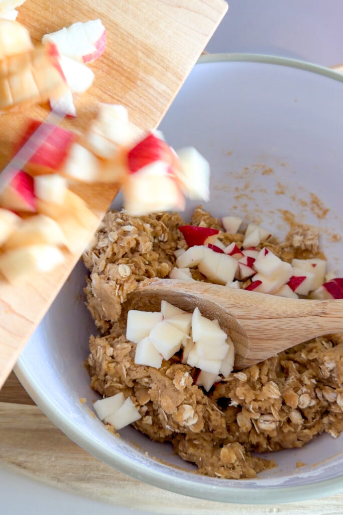 Adding diced apples to the crumble cookie dough mixture in a mixing bowl.