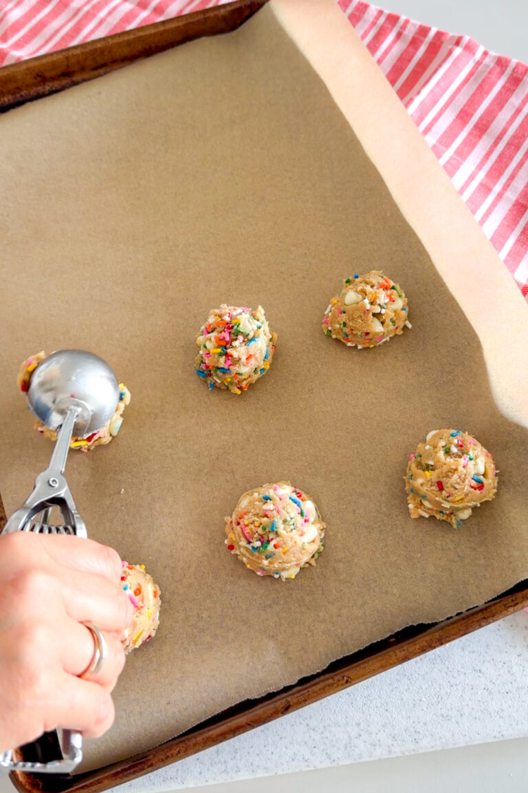 Using a cookie scoop to scoop mounds of Birthday Cake Cookies dough on a parchment-lined baking sheet