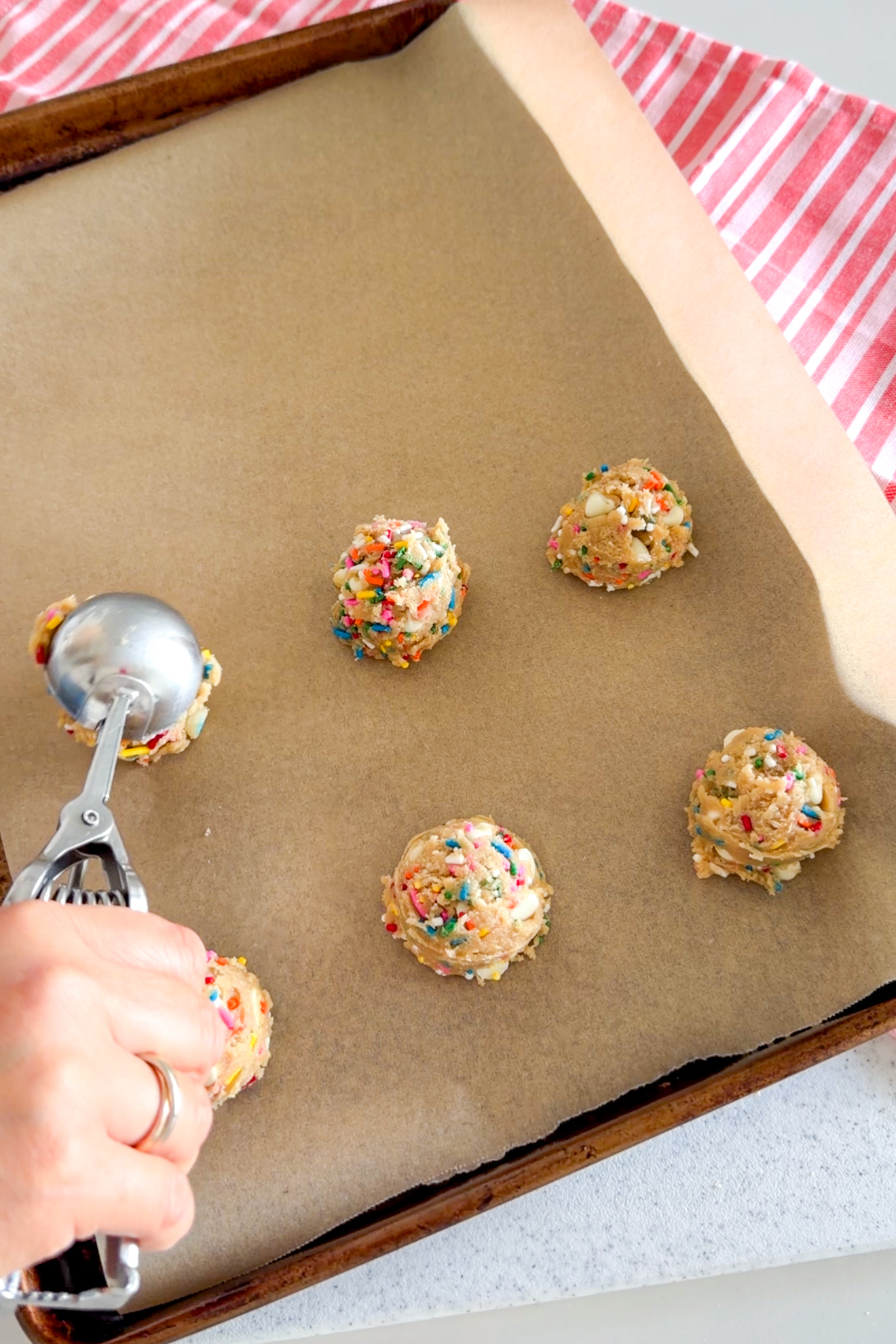 Using a cookie scoop to scoop mounds of Birthday Cake Cookies dough on a parchment-lined baking sheet