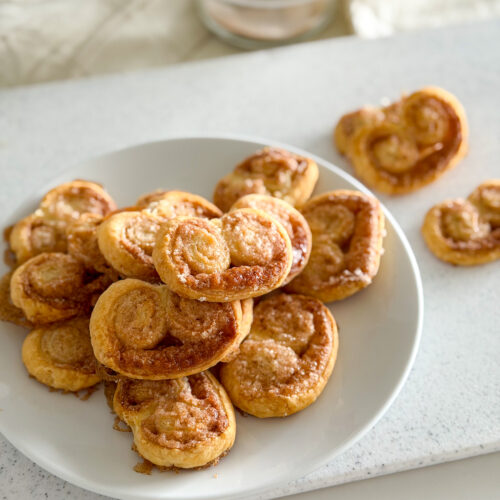 A plate of baked cinnamon palmiers arranged in a small pile.