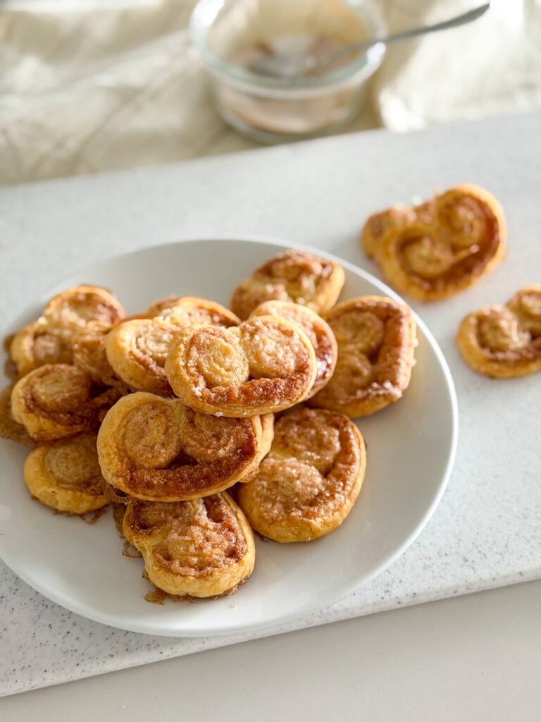 A plate of baked cinnamon palmiers arranged in a small pile.