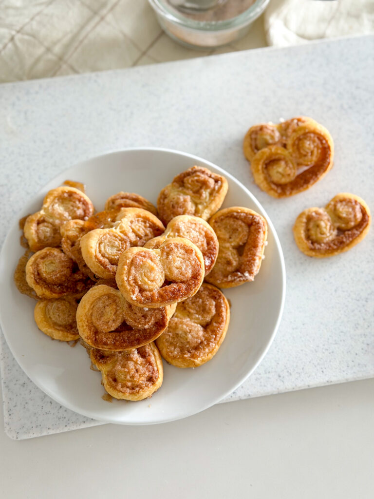 Close-up of golden, crispy cinnamon palmiers on a white plate.