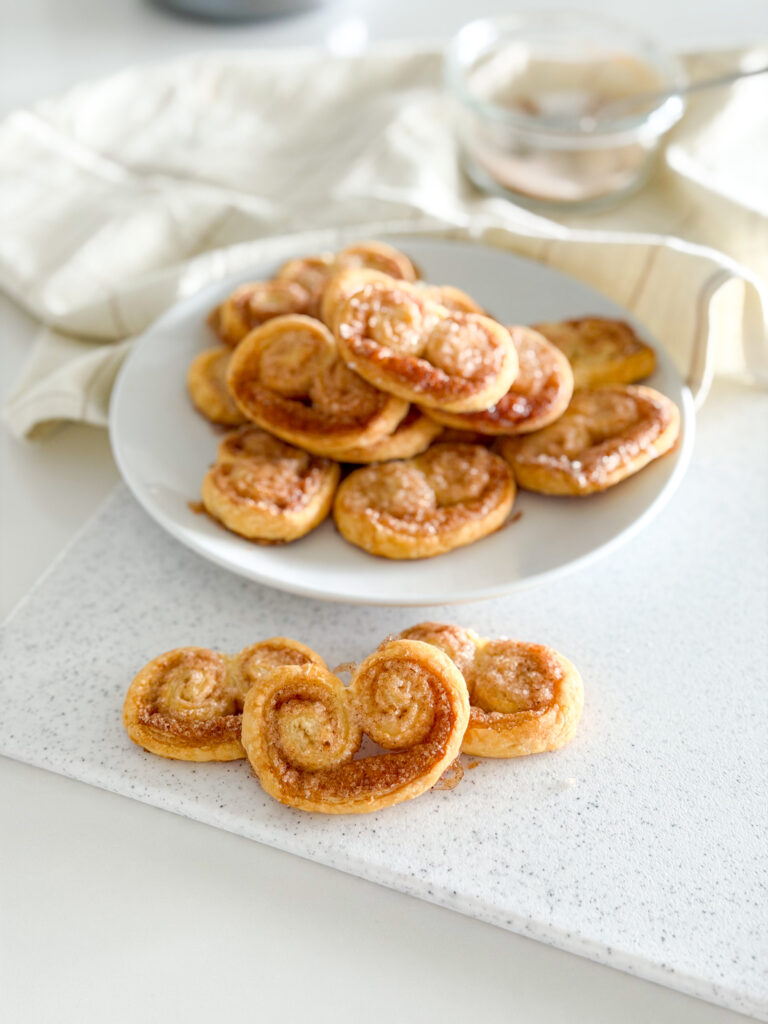 Close-up of golden, crispy cinnamon palmiers on a white plate.