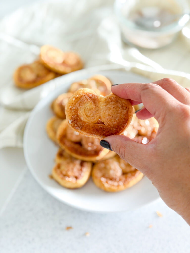 Hand holding a cinnamon palmier from a plate.