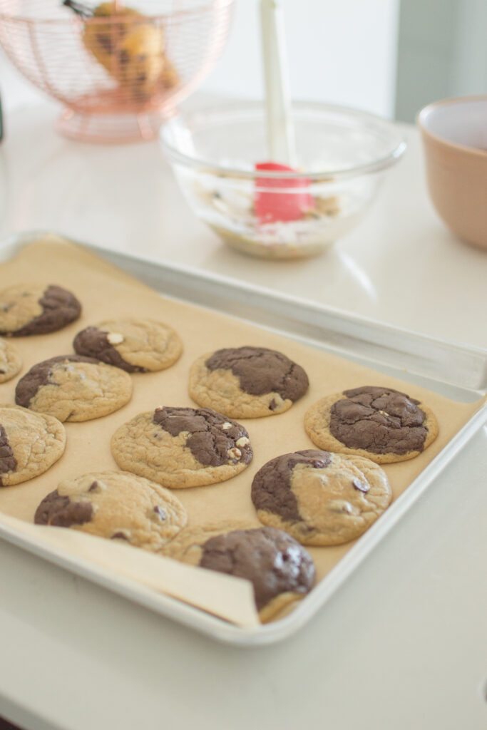 Half and half chocolate chip cookies baking on a parchment-lined tray