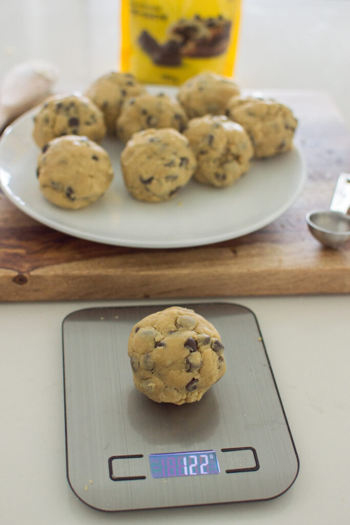 Large scoops of chocolate chip cookie dough being weighed for even baking